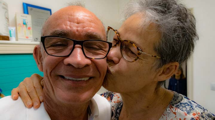 patient smiling with his wife kissing him after basal dental implant procedure